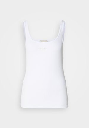 Bílý žebrovaný top s širokými ramínky a jemným světle béžovým logem Calvin Klein umístěným ve středu hrudi, zobrazený na jednobarevném pozadí.