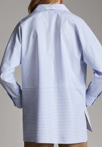 Gestreepte button-up shirt in lichtblauw en wit, met een relaxte pasvorm, wijde mouwen en zijsplitten voor optimaal draagcomfort.