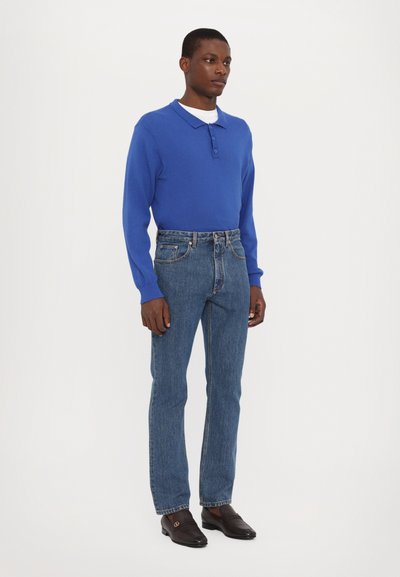 Blue long-sleeve polo shirt with button placket, paired with high-waisted dark denim jeans and black loafers. Simple, clean lines throughout.