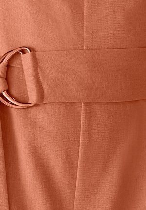 Primo piano di una cintura in tessuto color ruggine con texture, dotata di una fibbia a doppio anello in metallo color oro rosa, realizzata in tessuto abbinato.