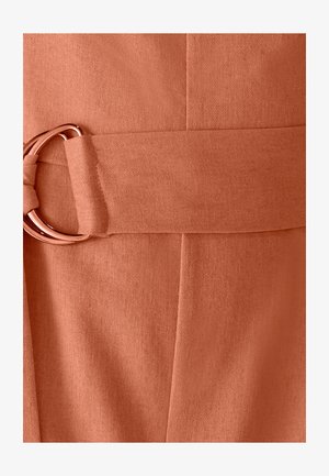 Nærbillede af et tekstureret støvfarvet bælte med et roseguld metal dobbelt ring spænde i matchende stof.