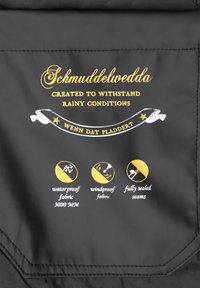 Melna ūdensizturīga auduma marķējums ar zelta tekstu. Simboli norāda uz ūdensizturību (3000 mm), vēja izturību un pilnībā noslēgtām šuvēm. Teksts lasāms kā "Schmuddelwedda."