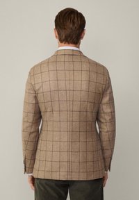 Blazer a quadri marrone realizzato in tessuto testurizzato; presenta una vestibilità strutturata, rever a coda di rondine e dettagli con polsini abbottonati.