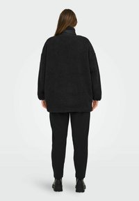 Czarny polarowy sweter z wysokim kołnierzem, w luźnym kroju i teksturowanej tkaninie. Nosi się go na czarnych spodniach i solidnym obuwiu.