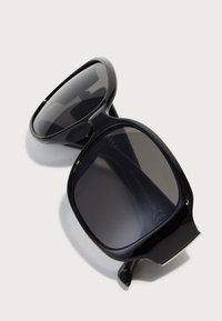 Schwarze übergroße Sonnenbrille mit dunkel getönten Gläsern, glattem Kunststoffrahmen und kantigem Design. Enthält dezente silberne Hardwareakzente.