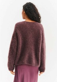 Sweter z długim rękawem o puszystej fakturze w bogatym kolorze mauve, z luźnym krojem i zaokrąglonym dekoltem, zestawiony z pasującą jedwabną spódnicą.