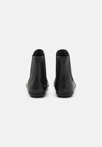 Botines de cuero negros con una textura suave, que presentan un tacón bajo y punta redondeada. La parte trasera incluye un discreto detalle del logo de la marca.