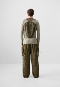 Olivgrünes Outdoor-Outfit mit einem Langarmoberteil und lockeren, cargo-stil Hosen mit mehreren Taschen und einem leichten, schichtbaren Design.