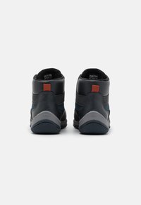 Zapatillas altas con parte superior de cuero negro, acentos grises y una etiqueta naranja. Superficies texturizadas y materiales en contraste para mayor soporte.