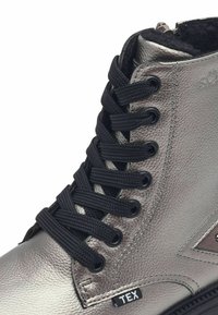 Bota alta metálica gris con cordones negros, cuero texturizado, detalle de cremallera y forro de tela. Presenta un logo y una etiqueta en el lado.