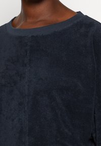 Camisa azul marino oscuro hecha de una tela suave con una textura lisa, con un escote redondo y costuras mínimas en los laterales.
