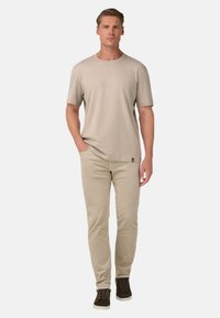 Krémové tričko s okrúhlym výstrihom v kombinácii s svetlo krémovými slim fit nohavicami. Oblečenie dopĺňajú tmavozelené vysoké tenisky. Hladká textúra po celom oblečení.