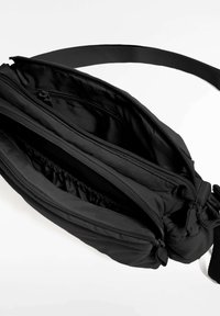 Črna najlonska ramenska torba z več predelki z zadrgo in nastavljivim trakom, s mehko, teksturirano površino.
