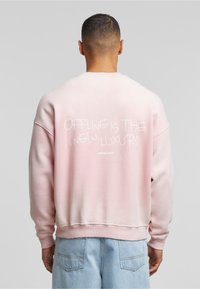 Felpa rosa con vestibilità rilassata, polsini a coste e stampa grafica sul retro. Realizzata in morbido cotone.