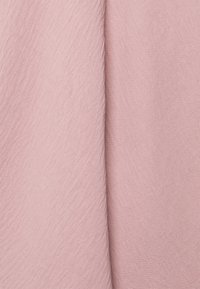 Texturerad rosa tyg med en något skrynklig yta, som visar en mjuk väv och subtila nyansvariationer.