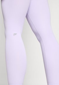 Leggings lilla realizzati in tessuto elasticizzato, con una texture liscia, design aderente e un piccolo logo stampato vicino al polpaccio.