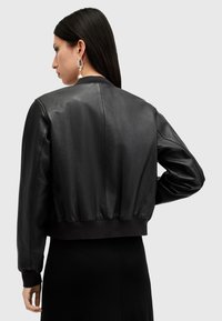 Chaqueta bomber de cuero negra con una silueta recortada, puños y dobladillo acanalados, y textura suave. Cuenta con un escote redondo y espalda sin costuras.