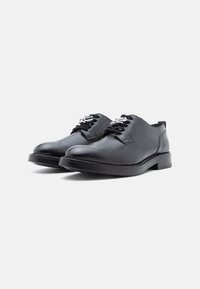 Sapatos de pele preta com atacadores, com acabamento liso, bico redondo e solas texturadas. Apresentam ilhós de metal prateado e atacadores pretos.