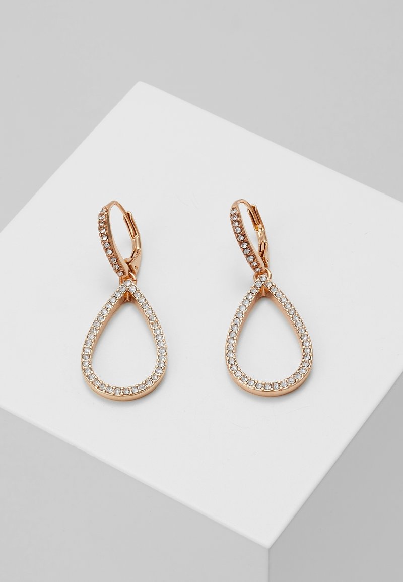 Boucles d'oreilles créoles en forme de goutte dorée avec de petits cristaux clairs délimitant les formes, exposées sur une surface blanche inclinée.
