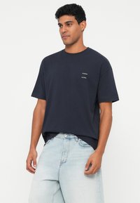 Ναυτικό μπλε βαμβακερό t-shirt με στρογγυλή λαιμόκοψη, κοντά μανίκια και δύο μικρά λευκά λογότυπα της μάρκας στο στήθος. Χαλαρή εφαρμογή.