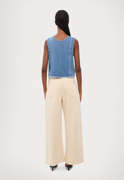 Džínová crop top s třepícími se okraji, spárovaná s béžovými kalhotami s vysokým pasem a širokými nohavicemi, které mají zadní kapsy a hladký povrch.