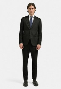 Svart kostym med skräddarsydd passform, enfingerknappskavaj och snibbkrage; matchad med en vit skjorta och mönstrat blått slips. Bärs med svarta kostymskor.