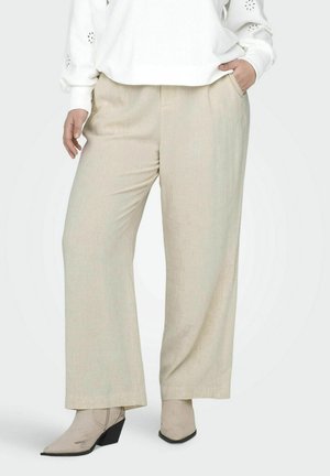 Pantalons larges beige en tissu texturé avec un léger éclat, dotés de poches latérales et d'une coupe décontractée, accompagnés de bottines beige.
