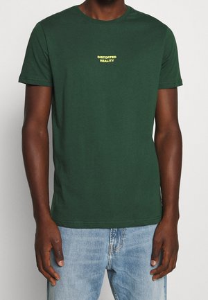 T-shirt en coton vert à manches courtes, col rond, avec l'inscription « DISTORTED REALITY » en lettres jaunes sur la poitrine. Coupe décontractée.