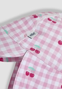 Rosa Vichykaro mit roten Kirschen. Mit weißen Nähten und einem kleinen Etikett mit der Aufschrift "ofo", das an der Kante angebracht ist.