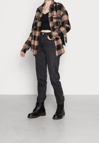 Buffalo-rutigt jacka i beige och svart, svart crop top, grå jeans och svarta snörstövlar med gula accenter. Minimalistisk handväska.