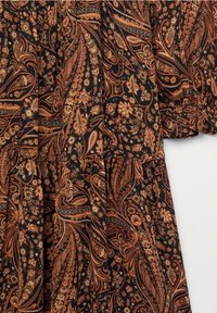 Tissu noir avec des motifs complexes de paisley et floraux dans des tons orange et marron, présentant un design délicatement froncé et une surface texturée.