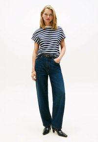 Top de rayas en azul marino y blanco de manga corta, combinado con jeans de pierna ancha de cintura alta en azul oscuro. Botines negros de tacón completan el look.