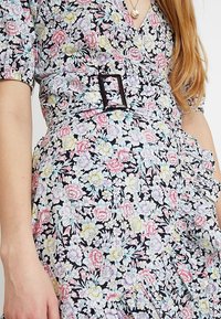 Vestido floral en negro con patrones coloridos de flores en rosa, amarillo y azul; cuenta con mangas abullonadas cortas y un elegante detalle de hebilla en el cinturón.
