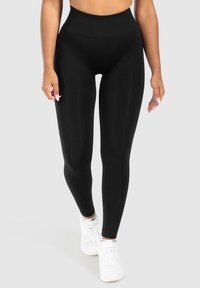  Hoge taille zwarte leggings gemaakt van een gladde, rekbare stof. Beschikt over een brede tailleband voor comfort, in combinatie met witte sportschoenen.
