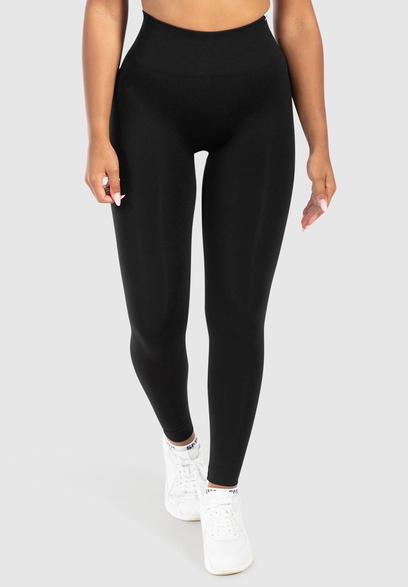  Hoge taille zwarte leggings gemaakt van een gladde, rekbare stof. Beschikt over een brede tailleband voor comfort, in combinatie met witte sportschoenen.