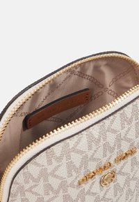 Bolso beige texturizado con herrajes dorados, que cuenta con un cierre de cremallera y una etiqueta de logo en el interior. El patrón incluye un sutil diseño geométrico.