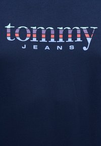 Ναυτικό μπλε βαμβακερό t-shirt με το όνομα της μάρκας "tommy" σε μεγάλα λευκά γράμματα, με πολύχρωμες οριζόντιες ρίγες από κάτω.