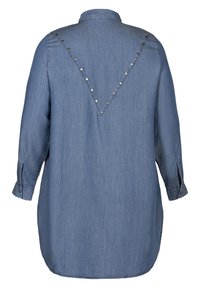 Chemise en denim à manches longues, avec un empiècement au dos présentant un motif en forme de V orné de clous, et un ourlet arrondi. Couleur bleu clair, texture lisse.