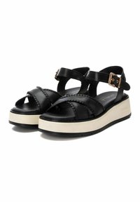 Sandalias de cuero negro con una suela de plataforma blanca gruesa. Presentan un detalle trenzado y correas ajustables con un acento de hebilla dorada.