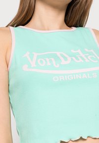 Mintgrön ribbad crop top med rosa kant som har "Von Dutch"-logotyp i vitt, råa fållar och en figurnära design.