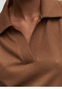 Polo shirt marron texturé avec un col classique et un motif côtelé subtil, mettant l'accent sur une palette de couleurs chaudes et des lignes épurées.