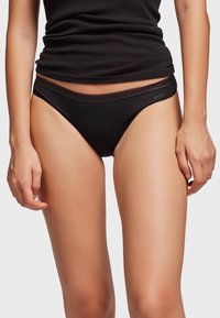 Crne bikini gaćice izrađene od glatkog materijala, s umjerenim prekrivanjem, čipkastim rubom oko struka i suptilnim logotipom brenda sa strane.