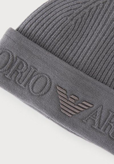 Bonnet en tricot côtelé gris avec revers plié comportant un texte de logo en relief et un emblème d'aigle stylisé embossé.