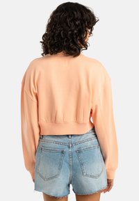 Przycięty różowy sweatshirt z opadającymi ramionami i prążkowym wykończeniem, zestawiony z jasnoniebieskimi szortami z przetartym denimu z kieszeniami naszytymi.