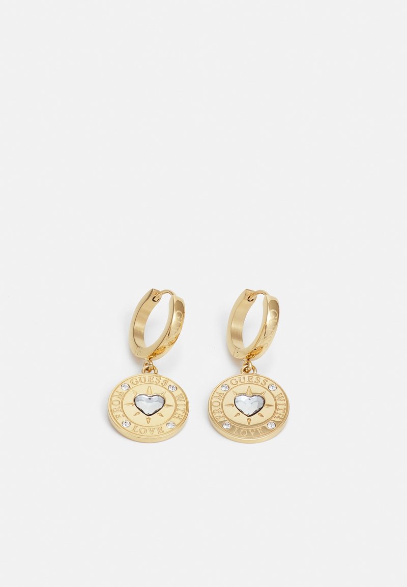 Boucles d'oreilles créoles en or avec des pendentifs ronds avec un centre en cristal en forme de cœur et le texte "Guess With Love" autour du bord.