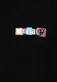 Svart bomulls-T-shirt med texten "LEGACY" i varierande färger och typsnitt, fastsatt som tygpatchar med en texturerad design.