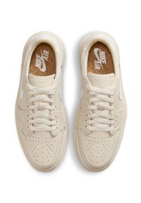 Nike Air tenisky ve světlé krémové kůži s perforovanou špičkou, kulatými tkaničkami a korkovou stélkou. Vyznačují se jemným logem na boku.