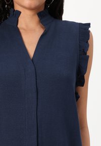 Top blu navy con colletto e bordi delle maniche arricciati, caratterizzato da scollatura a V e tessuto morbido. Design semplice senza motivi.