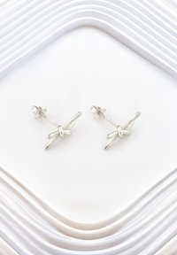 Söljda örhängen med en knutdesign som har släta, polerade ytor. Mot en vit, lager-på-lager bakgrund.