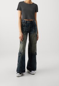 Černobílý krátký top s pruhy a vroubkovanými okraji, spárovaný s volnými modrými džínami s kapsami typu cargo a vybledlým vzhledem.